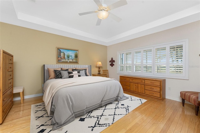 bedroom with light hardwood / wood-style flooring, ceiling fan, and a tray ceiling