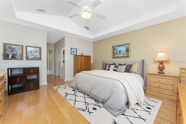 bedroom featuring connected bathroom, vaulted ceiling, light wood-type flooring, a raised ceiling, and ceiling fan