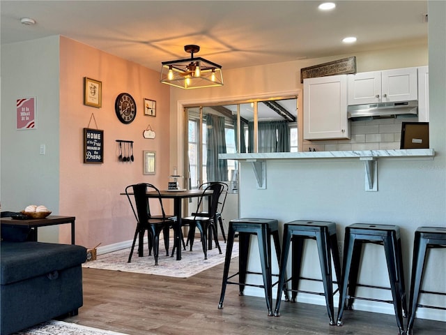 kitchen with white cabinetry, dark hardwood / wood-style flooring, a kitchen breakfast bar, kitchen peninsula, and decorative backsplash