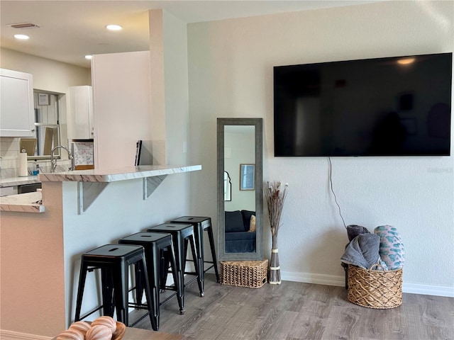 kitchen with a breakfast bar area, white cabinets, decorative backsplash, kitchen peninsula, and light wood-type flooring