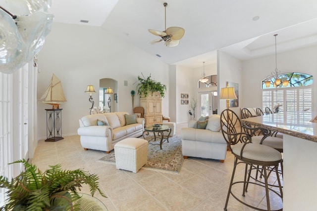 tiled living room with plenty of natural light, ceiling fan with notable chandelier, and high vaulted ceiling