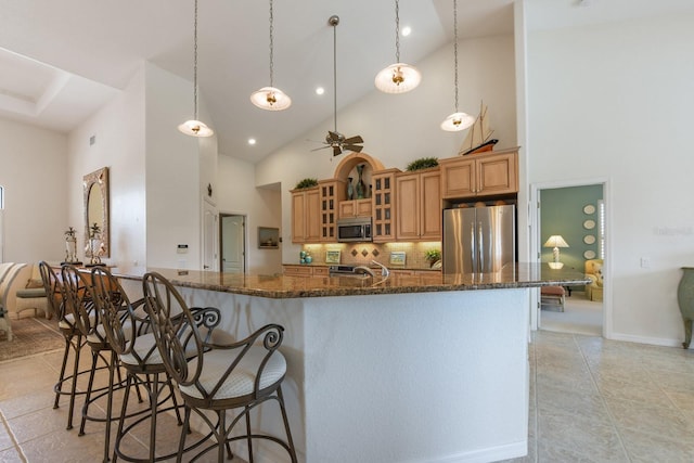 kitchen with pendant lighting, a breakfast bar area, ceiling fan, stainless steel appliances, and dark stone counters