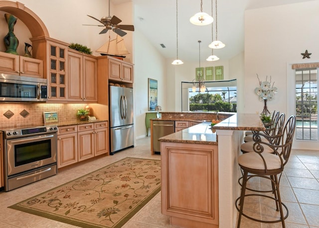 kitchen featuring pendant lighting, high vaulted ceiling, a kitchen island with sink, stainless steel appliances, and light stone countertops