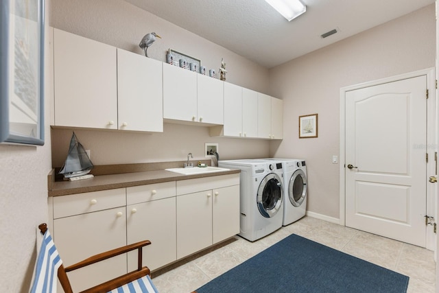 clothes washing area featuring sink, cabinets, a textured ceiling, washer and dryer, and light tile patterned floors