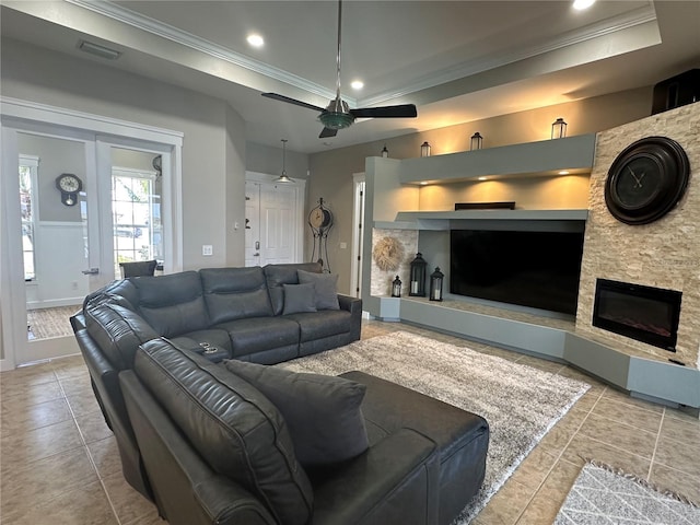 living area with a stone fireplace, recessed lighting, visible vents, ornamental molding, and a raised ceiling