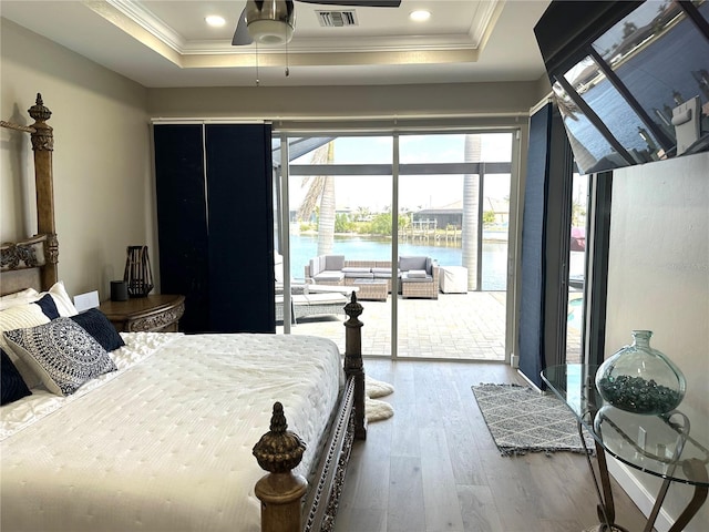 bedroom featuring crown molding, a raised ceiling, a water view, wood-type flooring, and access to outside