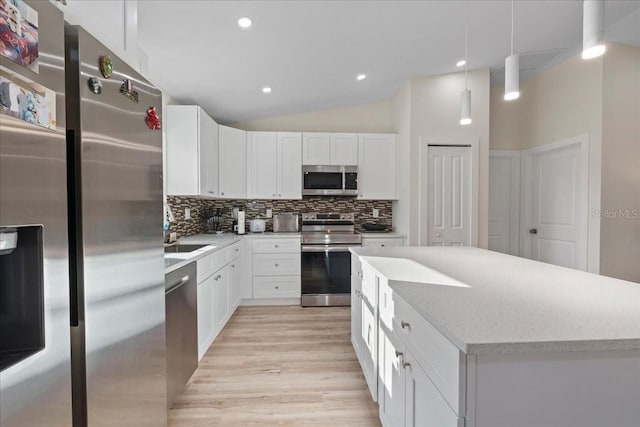 kitchen with appliances with stainless steel finishes, decorative light fixtures, white cabinets, backsplash, and light hardwood / wood-style floors