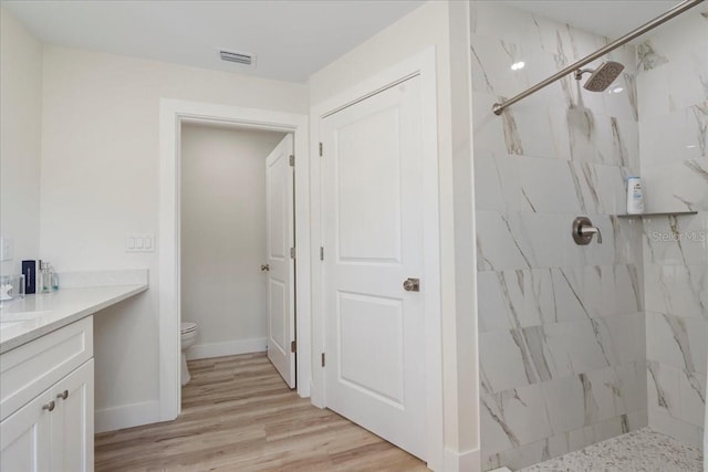 bathroom with hardwood / wood-style floors, vanity, a tile shower, and toilet