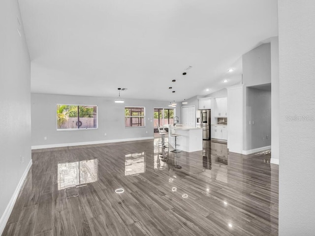 unfurnished living room featuring dark wood-style floors, lofted ceiling, a sink, and baseboards