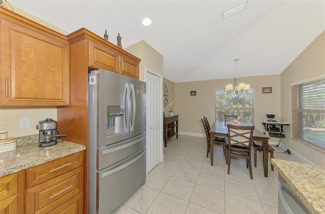 kitchen with vaulted ceiling, stainless steel fridge, light stone counters, and decorative light fixtures