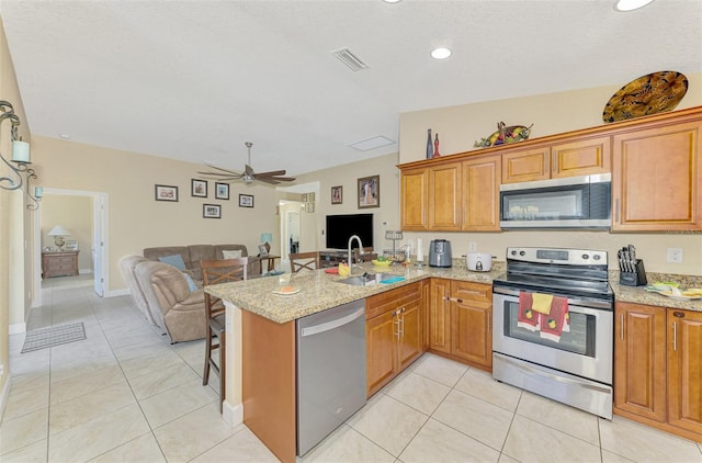 kitchen featuring sink, light tile patterned floors, appliances with stainless steel finishes, light stone counters, and kitchen peninsula