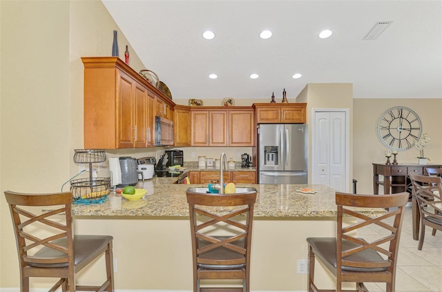 kitchen with appliances with stainless steel finishes, sink, a kitchen breakfast bar, kitchen peninsula, and light stone countertops