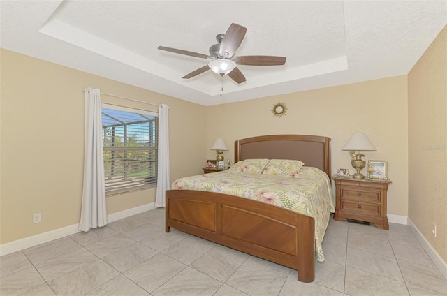 bedroom featuring ceiling fan, light tile patterned floors, a textured ceiling, and a tray ceiling