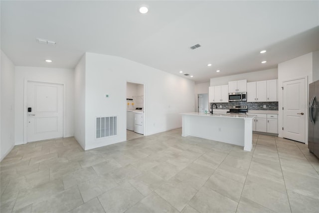 kitchen with sink, appliances with stainless steel finishes, a kitchen island with sink, white cabinets, and washer / dryer