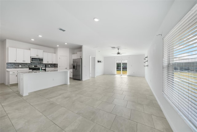 kitchen featuring an island with sink, white cabinets, ceiling fan, stainless steel appliances, and backsplash