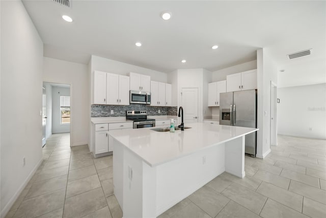 kitchen featuring sink, appliances with stainless steel finishes, tasteful backsplash, white cabinets, and a center island with sink