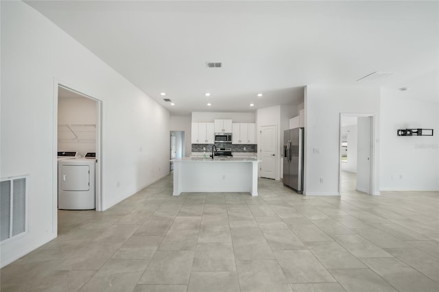 kitchen with separate washer and dryer, stainless steel appliances, a kitchen island with sink, decorative backsplash, and white cabinets