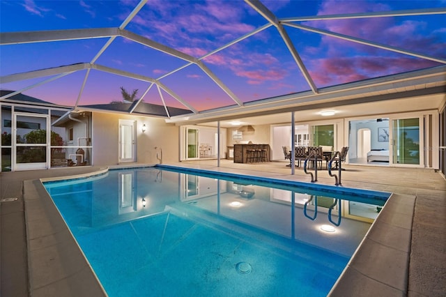 pool at dusk featuring a bar, a patio area, and glass enclosure