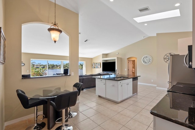 kitchen with sink, light tile patterned floors, appliances with stainless steel finishes, vaulted ceiling with skylight, and white cabinets