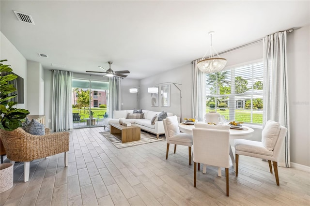 dining room with ceiling fan with notable chandelier, a wealth of natural light, and light hardwood / wood-style floors