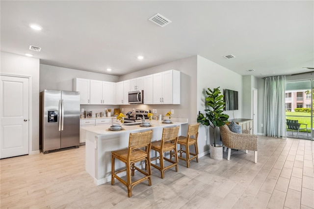 kitchen with light hardwood / wood-style flooring, appliances with stainless steel finishes, white cabinetry, a kitchen breakfast bar, and kitchen peninsula