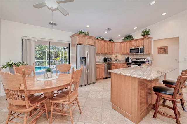 kitchen with ceiling fan, backsplash, stainless steel appliances, light stone countertops, and vaulted ceiling