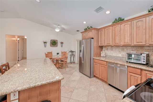 kitchen with lofted ceiling, a breakfast bar, appliances with stainless steel finishes, light stone countertops, and decorative backsplash