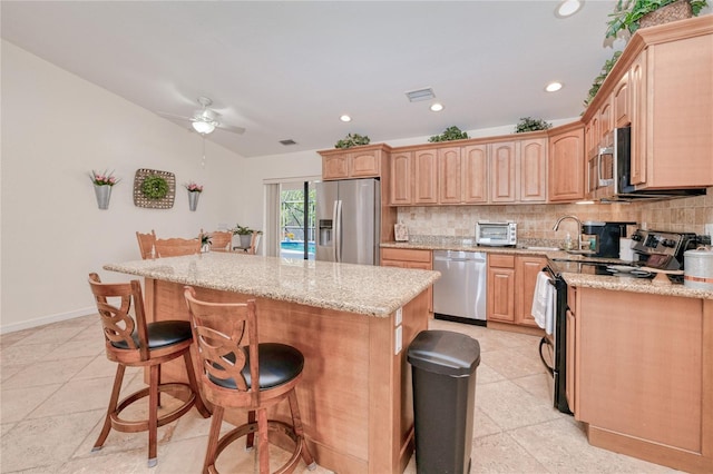 kitchen with appliances with stainless steel finishes, a kitchen breakfast bar, a kitchen island, light stone countertops, and backsplash