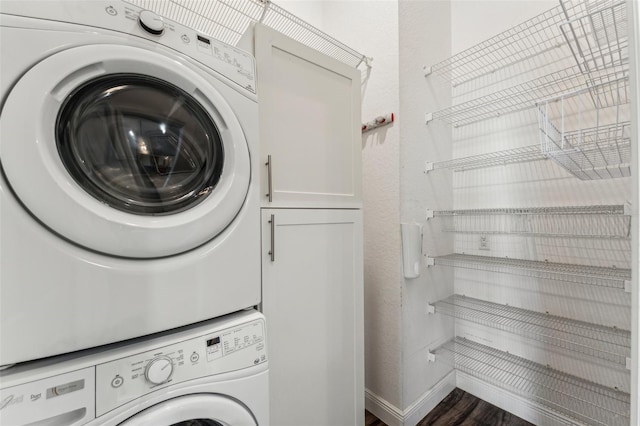 clothes washing area with dark wood-type flooring, cabinets, and stacked washer / dryer