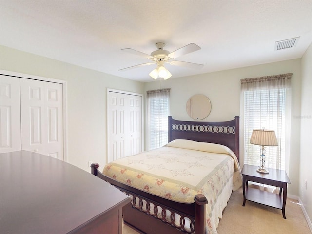 carpeted bedroom with multiple closets, ceiling fan, and multiple windows