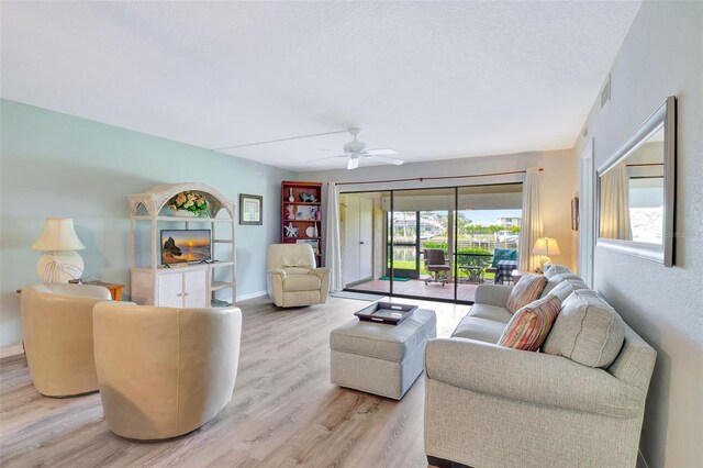 living room with light hardwood / wood-style flooring, ceiling fan, and a textured ceiling