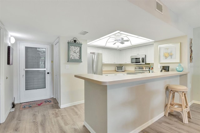 kitchen with kitchen peninsula, appliances with stainless steel finishes, white cabinets, and a breakfast bar