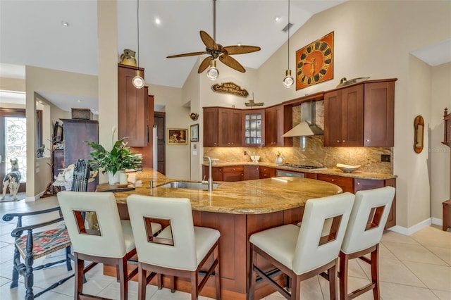 kitchen with wall chimney exhaust hood, a breakfast bar, sink, light stone counters, and kitchen peninsula