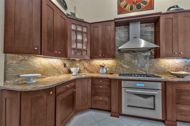 kitchen featuring sink, light stone counters, light tile patterned floors, white oven, and wall chimney range hood