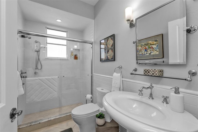 bathroom featuring sink, a shower with door, tile walls, tile patterned flooring, and toilet