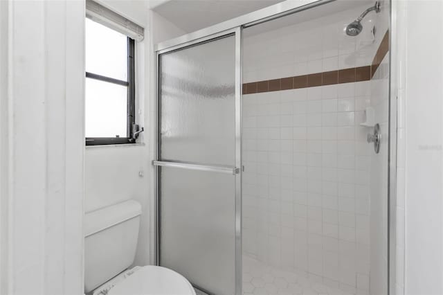 bathroom featuring a shower with door and toilet