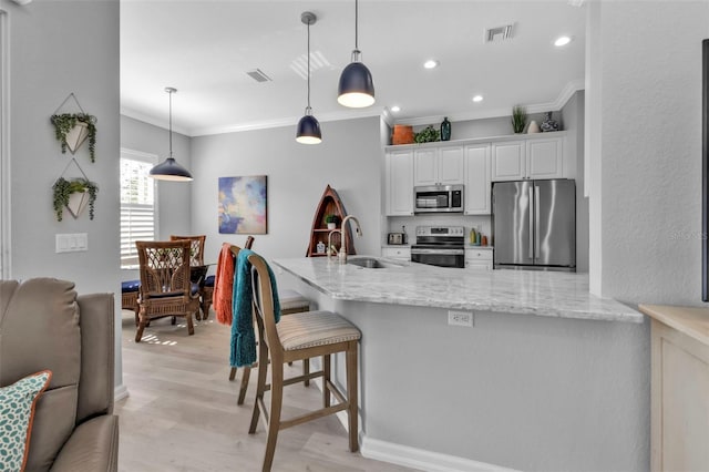 kitchen featuring stainless steel appliances, light stone counters, pendant lighting, sink, and white cabinetry