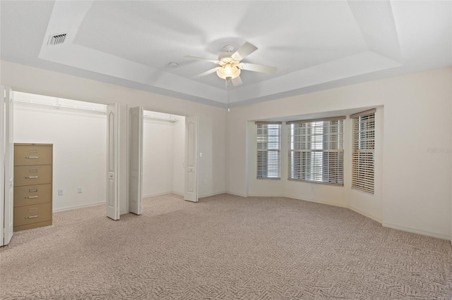 unfurnished bedroom with light colored carpet, a raised ceiling, and ceiling fan