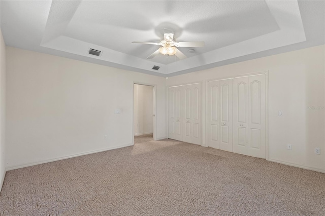 unfurnished bedroom with a raised ceiling, multiple closets, and light colored carpet