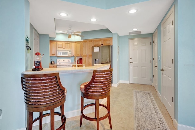 kitchen featuring a kitchen bar, ceiling fan, kitchen peninsula, light brown cabinets, and white appliances