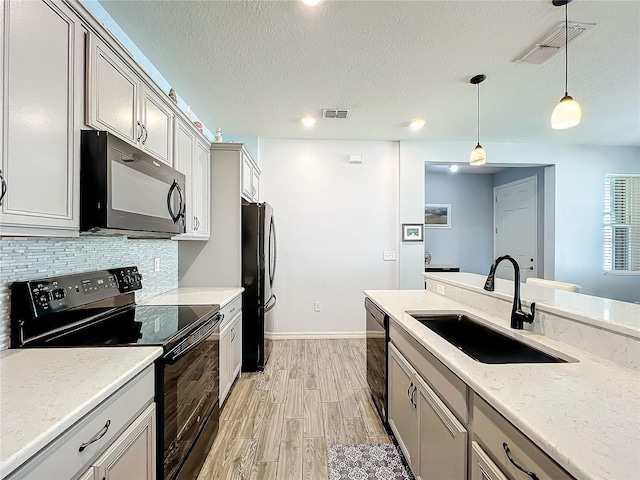 8858 Tuscany Isles Dr, Punta Gorda, FL 33950 - kitchen with tasteful backsplash, sink, hanging light fixtures, black appliances, and light hardwood / wood-style flooring