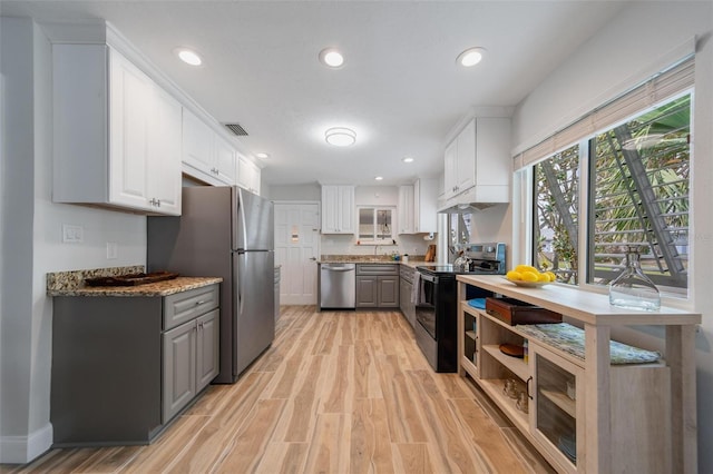 kitchen featuring dark stone countertops, light hardwood / wood-style flooring, white cabinetry, gray cabinetry, and stainless steel appliances