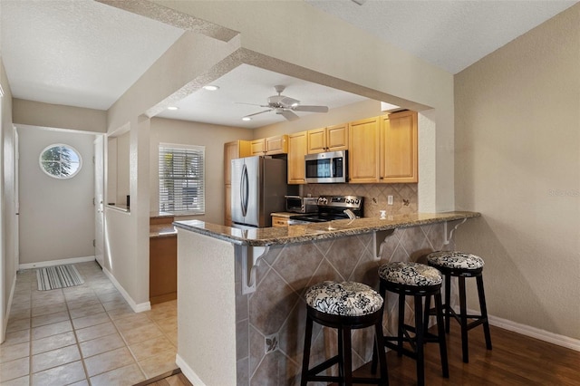 kitchen with stainless steel appliances, backsplash, a kitchen bar, and kitchen peninsula