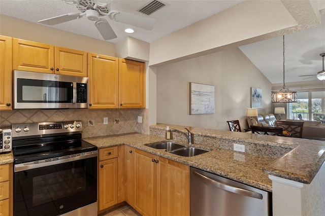 kitchen featuring sink, light stone counters, kitchen peninsula, stainless steel appliances, and decorative backsplash