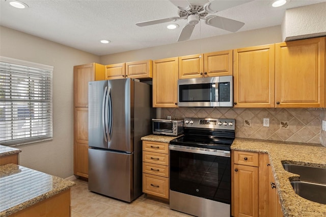 kitchen with light brown cabinetry, light stone counters, ceiling fan, stainless steel appliances, and backsplash