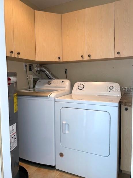 laundry area featuring washer and dryer, light tile patterned floors, cabinets, and electric water heater