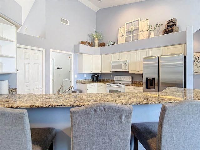 kitchen featuring a kitchen bar, white appliances, kitchen peninsula, and stone countertops