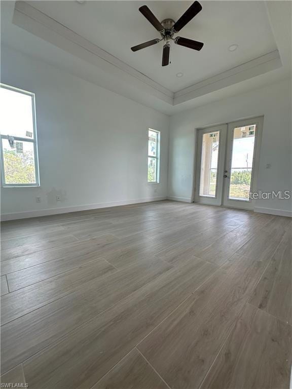 unfurnished room featuring light hardwood / wood-style flooring, ornamental molding, ceiling fan, a raised ceiling, and french doors