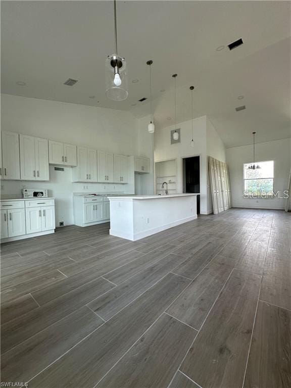 kitchen with dark wood-type flooring, sink, a center island with sink, a towering ceiling, and white cabinets