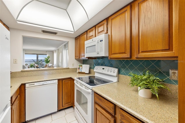 kitchen with light tile patterned flooring, white appliances, light stone countertops, and backsplash